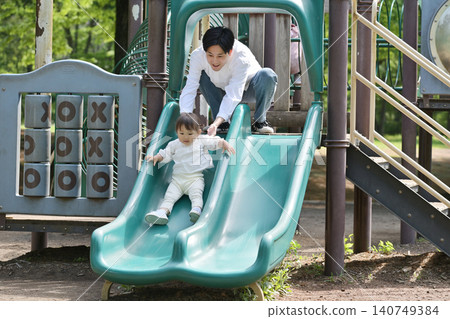 A daughter and her father enjoying a slide in the park. A daughter and her father enjoying a slide in the park. 140749384
