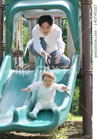女兒和父親在公園裡玩滑梯。 女兒和父親在公園裡玩滑梯。 140749387