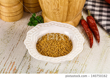 Mustard seeds in white ceramic bowl with dried red chili peppers and wooden kitchen tools on rustic table Mustard seeds in white ceramic bowl with dried red chili peppers and wooden kitchen tools on rustic table 140750162