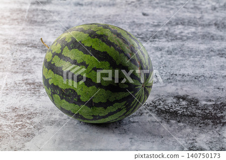 Whole watermelon with green and dark stripes on textured gray surface 140750173