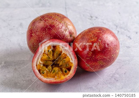 Fresh passion fruit with vibrant yellow pulp and red skin on light gray surface Fresh passion fruit with vibrant yellow pulp and red skin on light gray surface 140750185