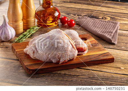 Raw chicken thighs on wooden cutting board with garlic rosemary olive oil and cherry tomatoes Raw chicken thighs on wooden cutting board with garlic rosemary olive oil and cherry tomatoes 140750231