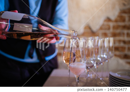 Professional waiter pouring rose sparkling wine into champagne flutes at an event Professional waiter pouring rose sparkling wine into champagne flutes at an event 140750477