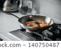 Shrimp sauteing in stainless steel pan on gas stovetop in home kitchen with fresh herbs and soft daylight, close-up view showing sizzling seafood and blurred background 140750487