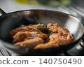 Golden-brown chicken pieces sizzling in black frying pan with fresh herb garnish, visible steam, crisp textured crust and warm kitchen lighting for appetizing home cooking scene 140750490