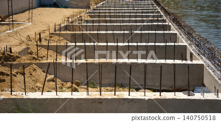Building process city levee. Exposed foundation rebar grid at site, standing formwork and concrete footings Building process city levee. Exposed foundation rebar grid at site, standing formwork and concrete footings 140750518