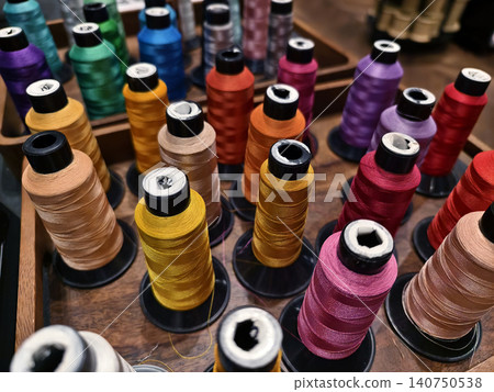 Colorful sewing thread spools arranged in wooden tray with shallow depth of field, glossy 140750538