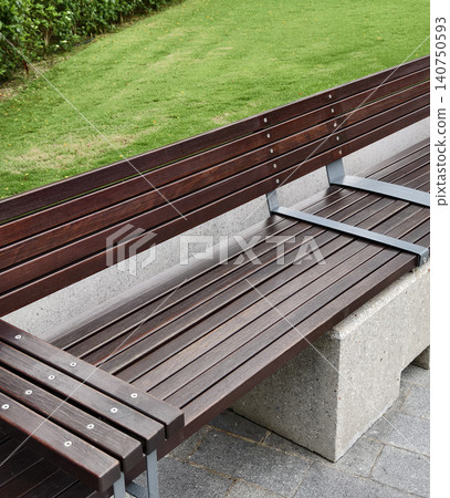 Solitary wooden bench on damp pavement with lush grass and subtle reflections post rainfall 140750593