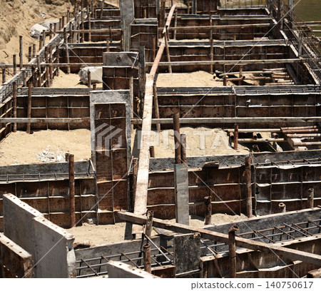 Building process city levee. Exposed foundation rebar grid at site, standing formwork and concrete footings Building process city levee. Exposed foundation rebar grid at site, standing formwork and concrete footings 140750617