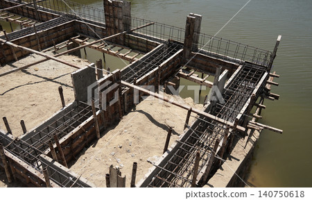 Building process city levee. Exposed foundation rebar grid at site, standing formwork and concrete footings Building process city levee. Exposed foundation rebar grid at site, standing formwork and concrete footings 140750618