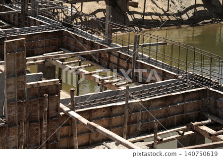 Building process city levee. Exposed foundation rebar grid at site, standing formwork and concrete footings Building process city levee. Exposed foundation rebar grid at site, standing formwork and concrete footings 140750619