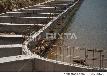 Building process city levee. Exposed foundation rebar grid at site, standing formwork and concrete footings Building process city levee. Exposed foundation rebar grid at site, standing formwork and concrete footings 140750622