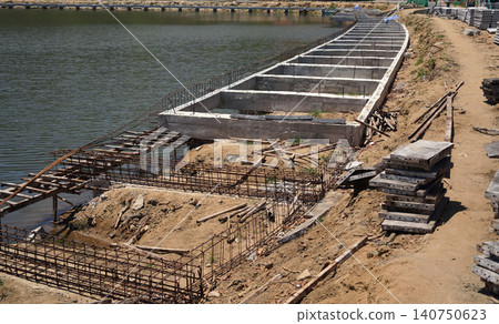 Building process city levee. Exposed foundation rebar grid at site, standing formwork and concrete footings Building process city levee. Exposed foundation rebar grid at site, standing formwork and concrete footings 140750623