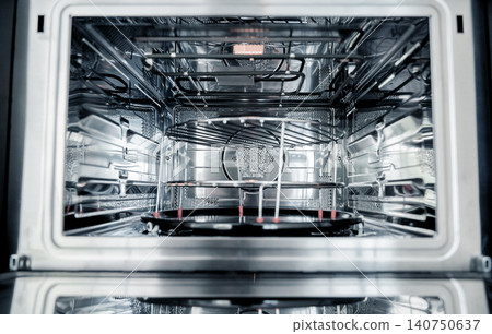 Open stainless oven interior with tray, clean metal rack and reflective glass door, warm lighting 140750637