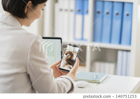 一位女商人利用工作間隙,透過智慧型手機查看愛犬的攝像頭,看看她不在家時狗狗的狀況。 (圖片) 一位女商人利用工作間隙,透過智慧型手機查看愛犬的攝像頭,看看她不在家時狗狗的狀況。 (圖片) 140751253