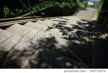畫面中,混凝土階梯沿著斜坡向下延伸,樹木的影子投射在扶手上。 畫面中,混凝土階梯沿著斜坡向下延伸,樹木的影子投射在扶手上。 140751974