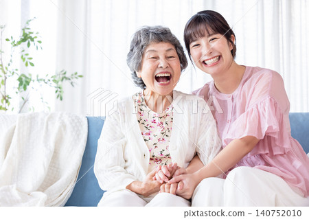A smiling senior woman and a young woman sitting on a sofa. A smiling senior woman and a young woman sitting on a sofa. 140752010