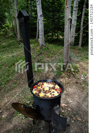Breakfast cooking in iron cauldron on outdoor burner in forest. Breakfast cooking in iron cauldron on outdoor burner in forest. 140752184