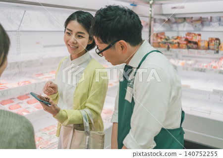 一位女顧客和一位店員在超市肉品區一起看智慧型手機。 一位女顧客和一位店員在超市肉品區一起看智慧型手機。 140752255