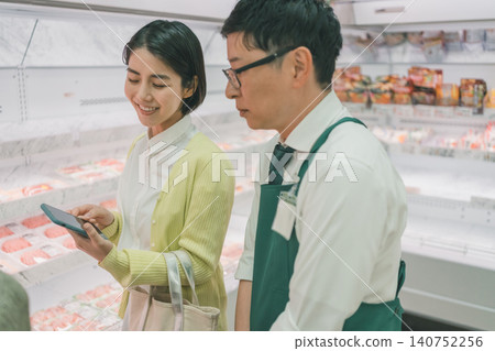 一位女顧客在超市肉品區一邊展示智慧型手機一邊微笑著聊天,而店員卻態度冷淡。 一位女顧客在超市肉品區一邊展示智慧型手機一邊微笑著聊天,而店員卻態度冷淡。 140752256