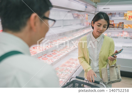 A female customer speaks to a store employee in the meat section of a supermarket. A female customer speaks to a store employee in the meat section of a supermarket. 140752258