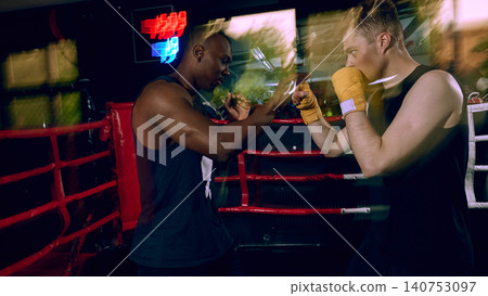 Boxing coach training athlete with hand wraps in dark boxing ring. 140753097