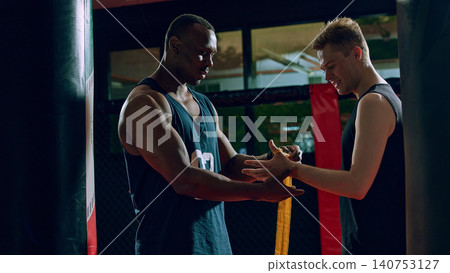 Coach helping boxer wrap hands before workout in dark training gym. Coach helping boxer wrap hands before workout in dark training gym. 140753127
