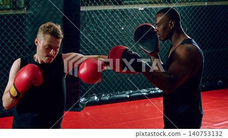 Focused boxer landing punch on trainer mitt during intense gym workout. Focused boxer landing punch on trainer mitt during intense gym workout. 140753132