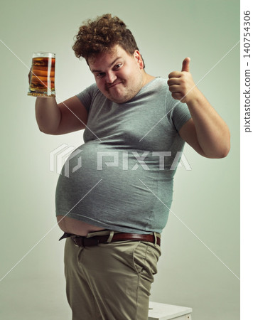 Plus size, portrait and thumbs up from man with beer for unhealthy habit, stomach and weight gain in studio of white background. Emoji, hand and male person by alcohol, funny face and calories Plus size, portrait and thumbs up from man with beer for unhealthy habit, stomach and weight gain in studio of white background. Emoji, hand and male person by alcohol, funny face and calories 140754306