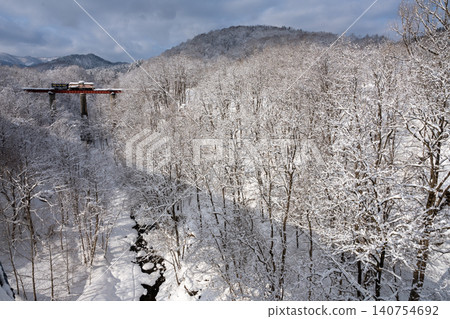 A winter scene of a snow-covered forest and a train crossing the Ashibetsu Bridge. A winter scene of a snow-covered forest and a train crossing the Ashibetsu Bridge. 140754692