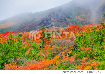 Under a cloudy autumn sky, the beautiful autumn foliage of Mount Kurikoma stretches endlessly down the valley, creating a stunning landscape of vibrant colors. Under a cloudy autumn sky, the beautiful autumn foliage of Mount Kurikoma stretches endlessly down the valley, creating a stunning landscape of vibrant colors. 140755733