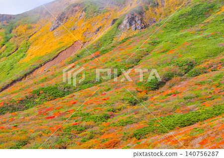 Under a cloudy autumn sky, Mount Kurikoma is at the peak of its autumn foliage – a close-up of the mountainside covered in beautiful, wave-like patterns of vibrant colors. Under a cloudy autumn sky, Mount Kurikoma is at the peak of its autumn foliage – a close-up of the mountainside covered in beautiful, wave-like patterns of vibrant colors. 140756287