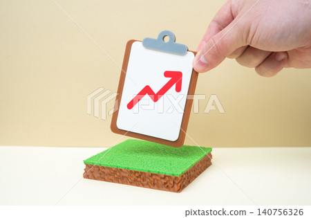 A plot of land and a tablet with a red arrow pointing upward. Rising land prices, increasing rental income. Land tax increases. 140756326