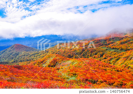 On a clear autumn day, Mount Kurikoma is at the peak of its autumn foliage, with glimpses of blue sky peeking through the clouds, creating a beautiful landscape of the entire mountain covered in vibrant autumn colors. On a clear autumn day, Mount Kurikoma is at the peak of its autumn foliage, with glimpses of blue sky peeking through the clouds, creating a beautiful landscape of the entire mountain covered in vibrant autumn colors. 140756474
