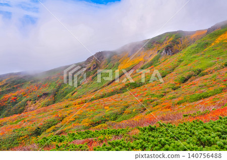 On a clear autumn day, Mount Kurikoma is at the peak of its autumn foliage, with glimpses of blue sky peeking through the clouds, creating a beautiful landscape of the entire mountain covered in vibrant autumn colors. On a clear autumn day, Mount Kurikoma is at the peak of its autumn foliage, with glimpses of blue sky peeking through the clouds, creating a beautiful landscape of the entire mountain covered in vibrant autumn colors. 140756488