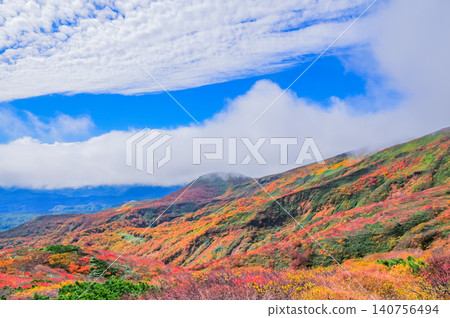 On a clear autumn day, Mount Kurikoma is at the peak of its autumn foliage, with glimpses of blue sky peeking through the clouds, creating a beautiful landscape of the entire mountain covered in vibrant autumn colors. On a clear autumn day, Mount Kurikoma is at the peak of its autumn foliage, with glimpses of blue sky peeking through the clouds, creating a beautiful landscape of the entire mountain covered in vibrant autumn colors. 140756494