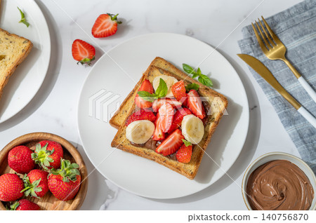 Toasted bread with chocolate cream, strawberries, and banana on a plate on a marble background Toasted bread with chocolate cream, strawberries, and banana on a plate on a marble background 140756870