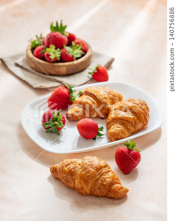 Freshly baked croissants on a plate with strawberries on a bright textured background. Freshly baked croissants on a plate with strawberries on a bright textured background. 140756886