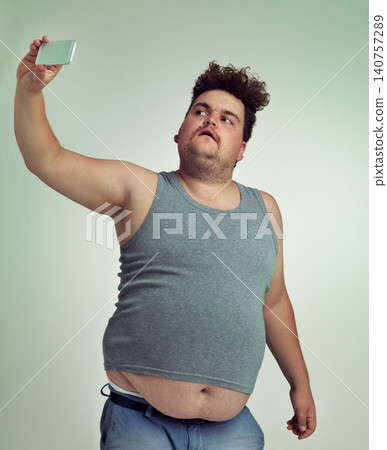 Selfie, fashion and plus size man in studio posing with casual, trendy and cool outfit with stomach. Style, serious and crazy male person with photography picture isolated by gray background. Selfie, fashion and plus size man in studio posing with casual, trendy and cool outfit with stomach. Style, serious and crazy male person with photography picture isolated by gray background. 140757289