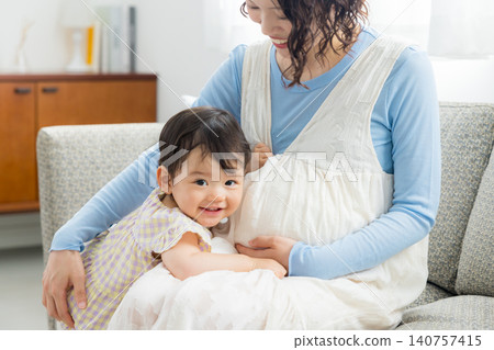 A pregnant mother holding her one-year-old daughter. A pregnant mother holding her one-year-old daughter. 140757415