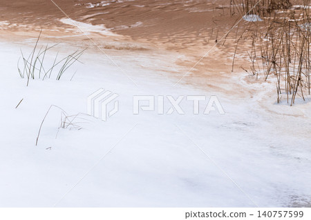 Snow blankets a quiet marsh as dried reeds rise from shoreline 140757599
