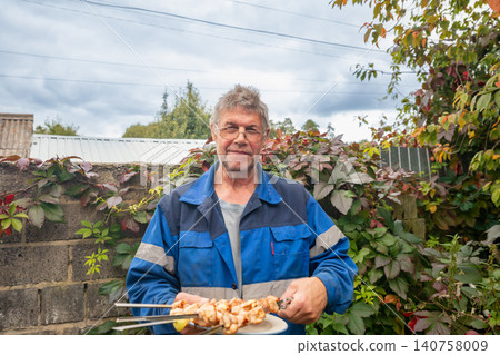 Farmer holding skewer with cooked meat shashlik outdoors. Man in work uniform enjoying barbecue meal. Rural lifestyle and food preparation concept for summer holiday celebration. 140758009