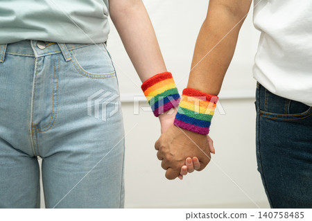Asian LGBT couple woman holding hand wearing rainbow wristband. Asian LGBT couple woman holding hand wearing rainbow wristband. 140758485