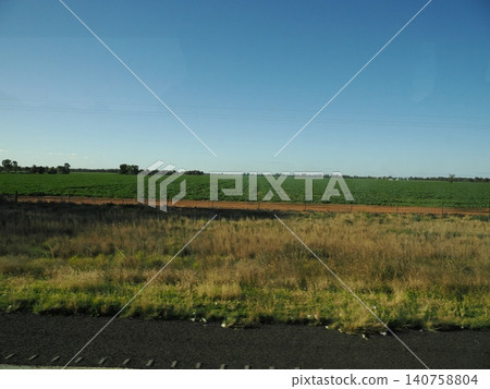 The scenery outside the train window presents a stark contrast between the dry foreground and the lush green farmland—a gentle journey where the landscape continues to change. 140758804