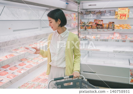 A female customer picks up a package of meat and examines it in the meat section of a supermarket. 140758931