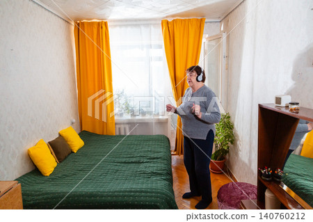Elderly woman performing light dance movements while listening to music at home. Fitness and wellness in retirement. Positive lifestyle concept. Wide shot Elderly woman performing light dance movements while listening to music at home. Fitness and wellness in retirement. Positive lifestyle concept. Wide shot 140760212