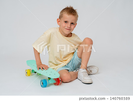 Horizontal studio shot of a calm and confident young boy sitting on the floor, leaning comfortably on his mint green skateboard. Clean white background with plenty of copy space. High-quality Horizontal studio shot of a calm and confident young boy sitting on the floor, leaning comfortably on his mint green skateboard. Clean white background with plenty of copy space. High-quality 140760389