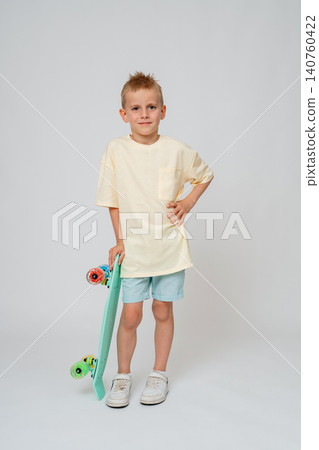 Full length studio shot of a calm preteen boy standing straight, holding a mint green skateboard vertically with one hand. Clean minimalist background, perfect for commercial advertising. Confident Full length studio shot of a calm preteen boy standing straight, holding a mint green skateboard vertically with one hand. Clean minimalist background, perfect for commercial advertising. Confident 140760422