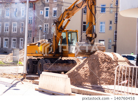 Construction workers preparing site before sidewalk paving. Excavator moves sand piles. Urban development in progress. City infrastructure improvement for better pedestrian walkways 140760458