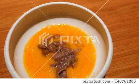 close up of Japanese Sukiyaki hot pot wagyu beef slice in a rich orange raw egg yolk broth sauce in a white bowl on a wooden table with copy space close up of Japanese Sukiyaki hot pot wagyu beef slice in a rich orange raw egg yolk broth sauce in a white bowl on a wooden table with copy space 140761000